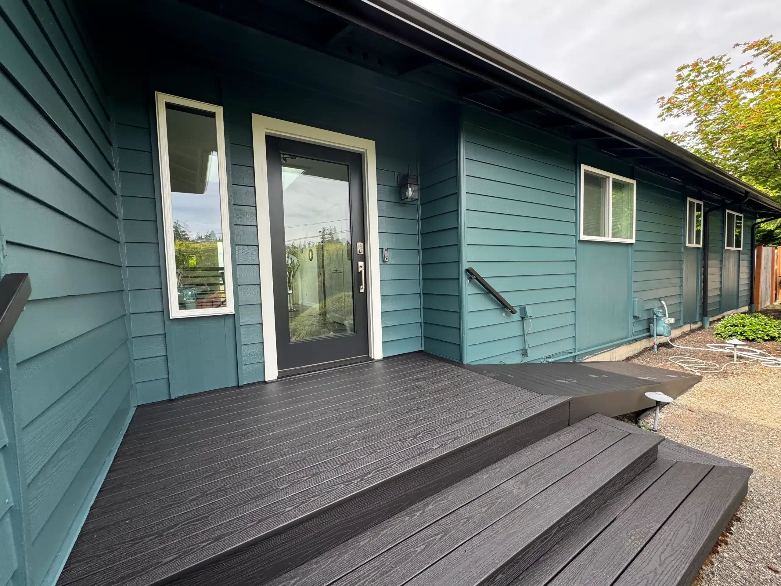 Teal Horizontal Siding Residential Home Teal-painted horizontal siding residential home exterior with dark composite deck, white-trimmed entry door, and black