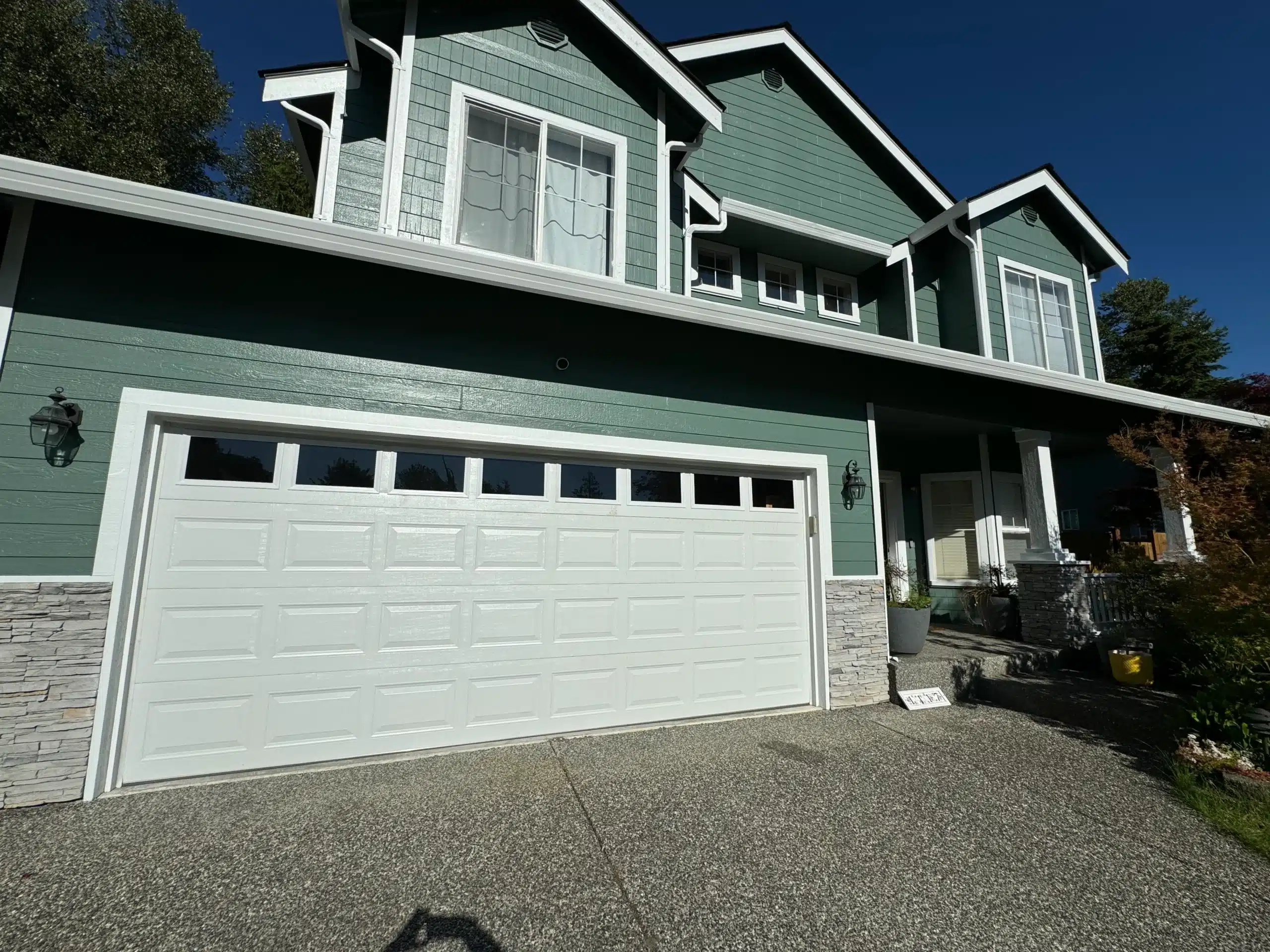 Sage Green Residential Home Exterior Sage green horizontal siding two-story residential home with white trim, white garage door, and stone veneer base in