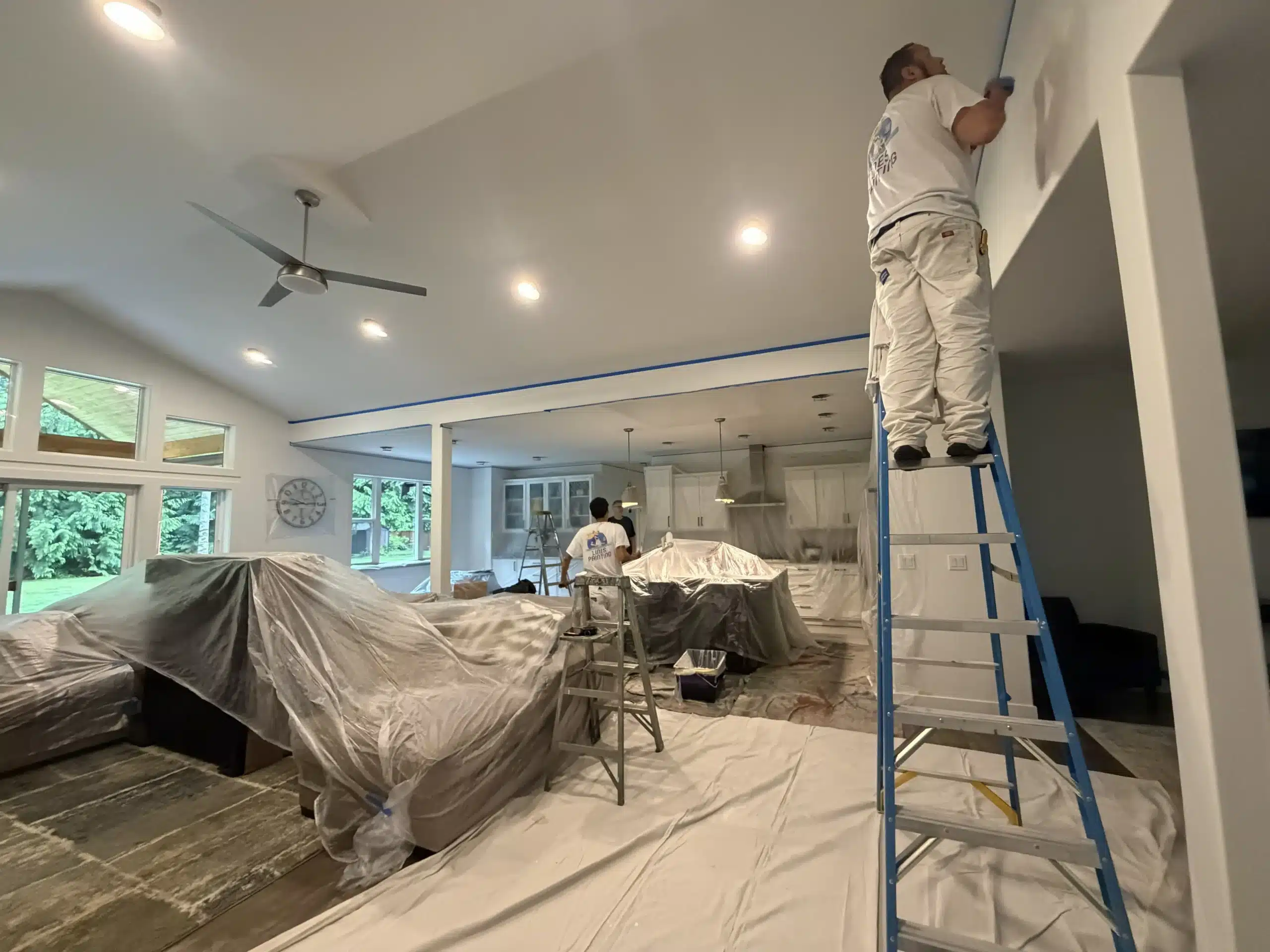 Expert residential painters transform open concept living spaces Professional painters carefully preparing and painting the interior walls of a large, open concept living room and kitchen area.