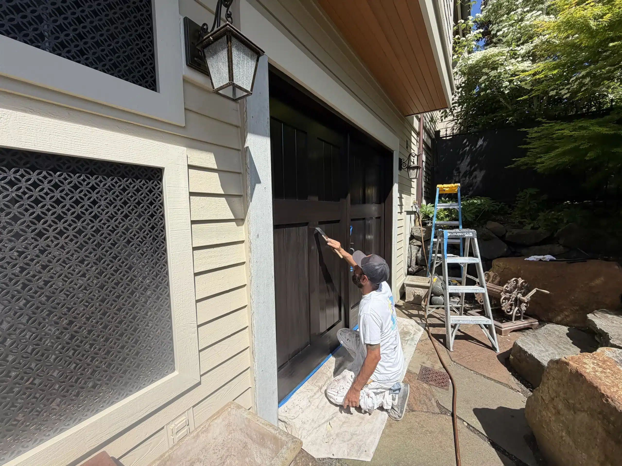 Expert garage door painting enhances home curb appeal A professional painter carefully applies dark brown paint to a residential garage door, enhancing the home's exterior curb appeal.