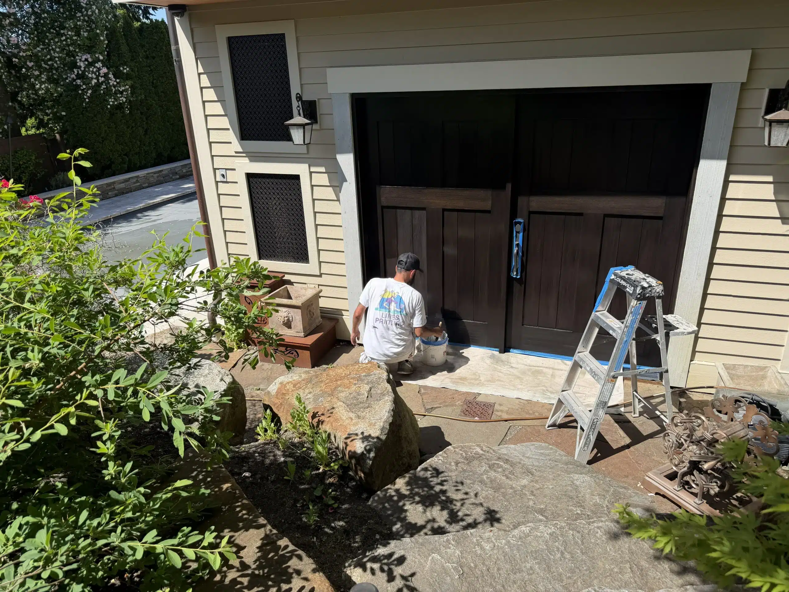 Professional painter applies fresh coat to a dark brown garage door A professional painter meticulously applies a fresh coat of dark brown paint to a residential garage door.