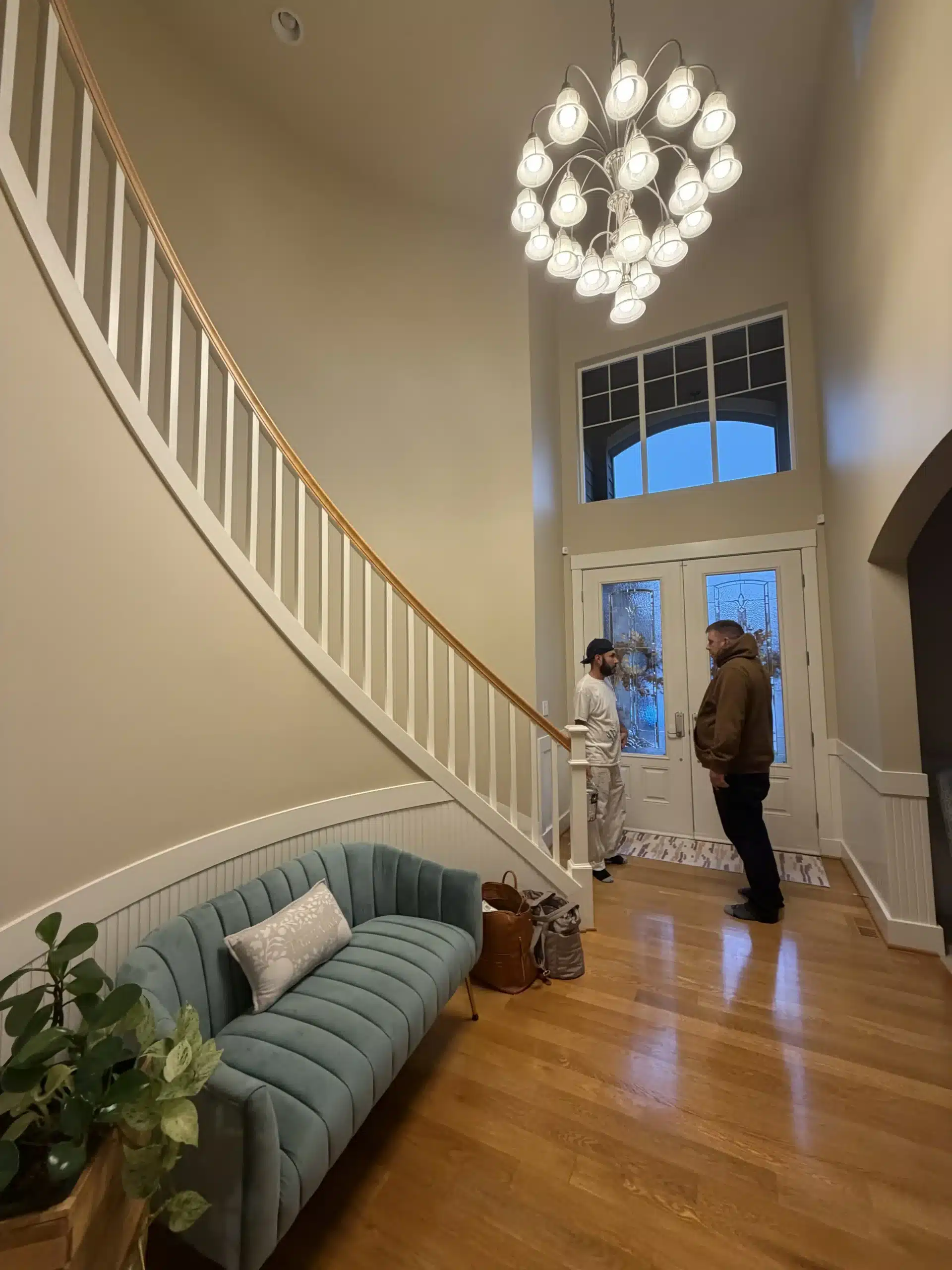 Professional Interior Painting Consultation for a Grand Entryway Two professionals discussing an interior painting project in a grand home entryway with a stunning curved staircase and high ceilings.